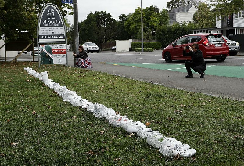 People photograph a memorial Monday of 50 pairs of white shoes for the victims of Friday’s mosque shootings in front of a church in Christchurch, New Zealand.