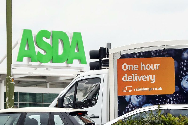 A Sainsbury’s grocery delivery van passes in front of an Asda supermarket last April in Watford, England. 