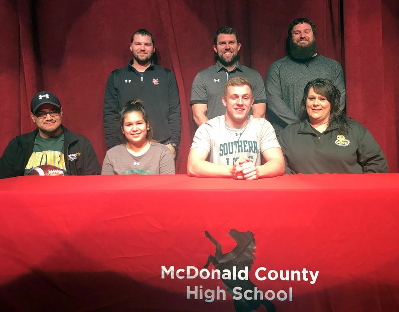 RICK PECK/SPECIAL TO MCDONALD COUNTY PRESS Micah Burkholder recently signed to play football at Missouri Southern State University in Joplin. Shown above at the signing are (front, left) Carlos Diaz (dad), Malia Diaz (sister), Micah Burkholder and Heather Burkholder (mom), and (back, left) MCHS coaches Kanon Hoover, Kellen Hoover and Craig Collins.