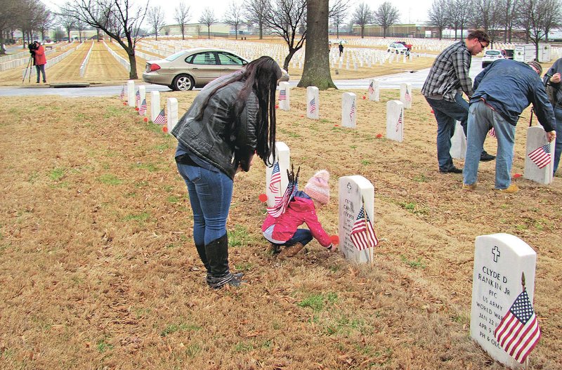 Addison Hale, 3, and her mother Elizabeth place a red flower on a grave at the Fort Smith National Cemetery Wednesday. The two were among about 25 who endured the drizzly morning to join Preston Sharp in honoring veterans. Sharp, 13, of Redding, Calif., travels the nation advocating the placement of flags and flowers at national cemeteries to honor veterans every day, not just on holidays. Sharp was recognized by President Donald Trump at his State of the Union address for his efforts to honor veterans.