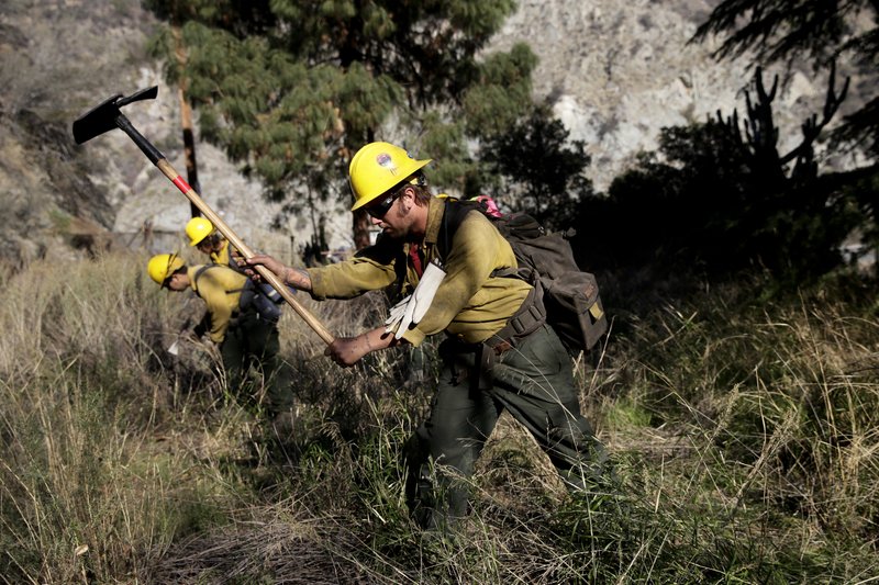 In this Jan. 17, 20014 file photo, firefighters clear brush as they battle the Colby Fire near Azusa, Calif. California is calling in the National Guard for the first time to help protect communities from wildfires like the one that destroyed much of the city of Paradise last fall. The state is pulling the troops away from President Donald Trump's border protection efforts in April 2019 and devoting them to fire protection, another area where the president has been critical of California officials. (AP Photo/Jae C. Hong, File)