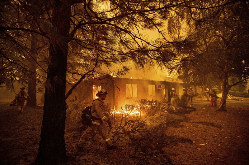 FILE - In this Nov. 9, 2018, file photo firefighters work to keep flames from spreading through the Shadowbrook apartment complex as a wildfire burns through Paradise, Calif. California is calling in the National Guard for the first time to help protect communities from wildfires like the one that destroyed much of the city of Paradise last fall. Starting in April 2019, 110 California National Guard troops will receive 11 days of training in using shovels, rakes and chain saws to thin trees and brush. (AP Photo/Noah Berger, File)