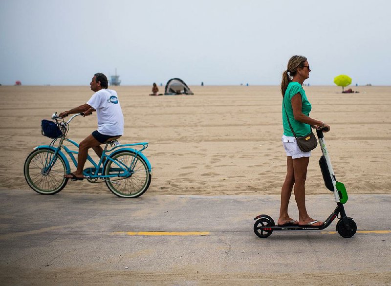 A rider on a Lime electric scooter passes a cyclist on the Venice Beach boardwalk in Los Angeles. 