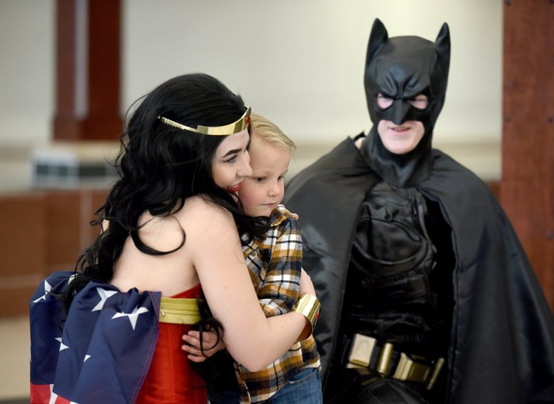 NWA Democrat-Gazette/DAVID GOTTSCHALK Miles McJunkin, 5, receives a hug Thursday from costumed superhero Wonder Woman as she kneels with Batman during Superhero Day at The Jones Center in Springdale. The center has held a variety of activities daily during Spring Break. Friday will feature the princesses from the animated film Frozen during Frozen Friday on the ice skating rink at the center.