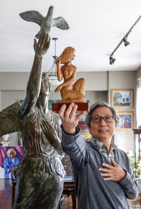 Longhua Xu holds his woodcarving, "Fishing Woman," in front of his bronze sculpture Eternal Hope in his Hot Springs studio. Xu is this year’s Arkansas Arts Council’s Living Treasure. (Arkansas Democrat-Gazette/JOHN SYKES JR.)