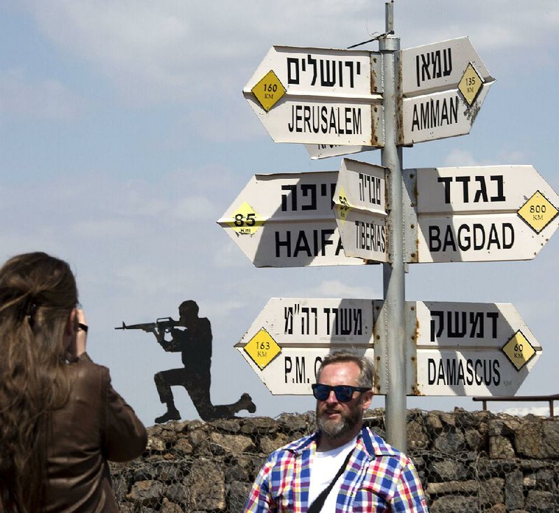 A tourist poses Friday next to a cutout of a soldier and a mock road sign for cities in the Middle East at an old outpost in the Israeli-controlled Golan Heights near the border with Syria.