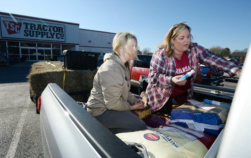 Tonya Bryant (right) of Prairie Grove and her daughter, Shai Bryant, write messages about Nebraska with shoe polish Thursday, March 21, 2019, on their pickup while seeking donations of livestock supplies and feed at Tractor Supply in Farmington before heading out to Elkhorn, Neb., to assist in flooding recovery. Bryant plans to return to collect more feed and veterinarian supplies from 8 to 10 a.m. Saturday at Tractor Supply in Farmington before driving back to Nebraska. Atwoods in Lowell has also joined in the effort. Bryant is working with No Town Left Behind and Guiding Spirit Animal Rescue Organization in her efforts and plans to make as many trips as necessary until people stop making donations.