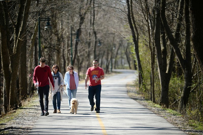 NWA Democrat-Gazette/ANDY SHUPE Nahum Payne (from left), Shawn Frick, Sydney Walsh and Jacob Meisenbacher, all co-workers at Creative in Fayetteville, walk Friday with Jackson along the trail west of the Fayetteville Public Library. Voters will be asked April 9 to continue the city's 1-cent sales tax to pay for about $226 million in projects. Of that, about $30 million would go toward building an arts corridor and parking downtown. Part of the arts corridor plan includes turning the Fay Jones Parkland woods into a natural attraction with a canopy walk, trail connections and restored vegetation and streamside areas.
