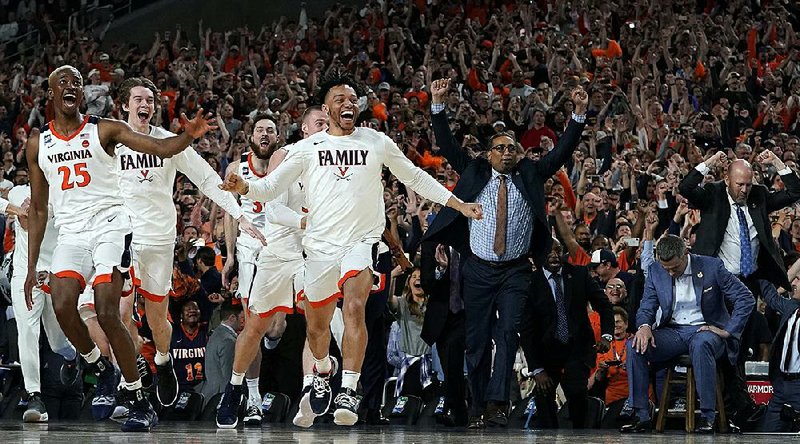 Virginia players and coaches, including head Coach Tony Bennett (far right, sitting), celebrate after defeating Texas Tech 85-77 in overtime in the NCAA Men’s Tournament championship Monday night in Minneapolis.