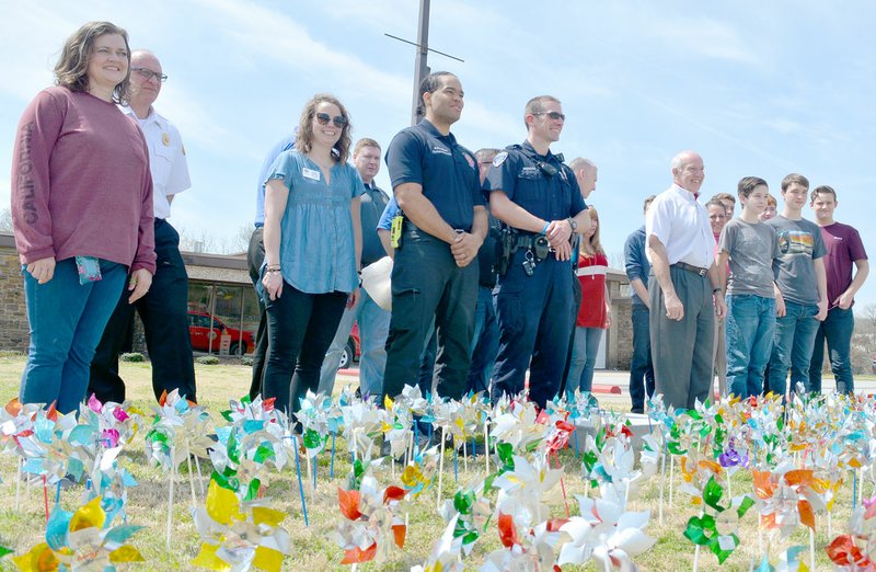 Keith Bryant/The Weekly Vista Bella Vista police and fire staff stand with Children's Advocacy Center of Benton County personnel, Eclectic Teaching Consortium of Northwest Arkansas students and Mayor Peter Christie after placing pinwheels in front of the police and fire departments' main entrances.