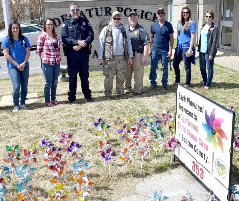 Westside Eagle Observer/MIKE ECKELS A group of local officials, police officers and volunteers gather in front of a sign representing the number of confirmed child abuse cases in Benton County April 5. The group planted 353 pinwheels in front of the Decatur Police Station in Decatur. Participating in the event were Early Mallow (left), Sheila Verser, Stephen Grizzle, Randy Cox, Joe Savage, Troy Wackes, Erin Kramer and Taylor Fairchild.