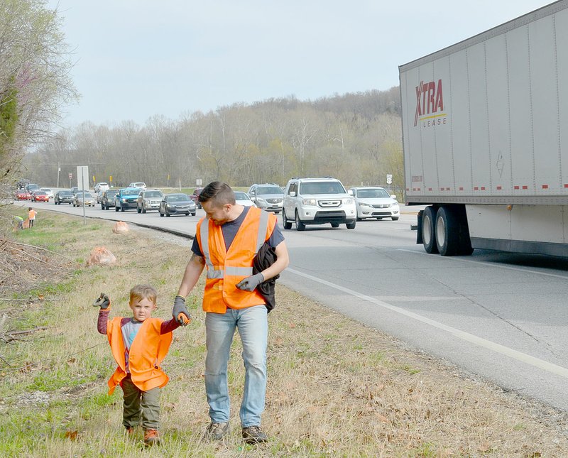 Keith Bryant/The Weekly Vista Cypress Wakefield (left), 3, holds up a steel shackle he found alongside the interstate while Jason Wakefield walks with him along U.S. Highway 71, just north of its intersection with Benton County Road 40.