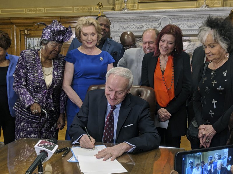 Arkansas Gov. Asa Hutchinson signs a bill into law that replaces the state's two statues in a U.S. Capitol display with statues of civil rights leader Daisy Bates and country musician Johnny Cash, Thursday, April 11, 2019, in Little Rock, Ark. The governor was joined by friends and family of Bates and Cash, including the singer's daughter, musician Rosanne Cash, and the activist's goddaughter, Jan Brown. The Bates and Cash statues in the Capitol's National Statuary Hall Collection will replace statues of attorney Uriah Milton Rose and former Gov. and Sen. James Paul Clarke. (AP Photo/Hannah Grabenstein)