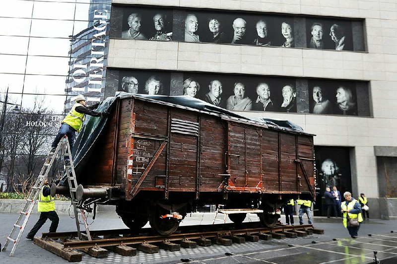 Portraits of Holocaust survivors are displayed at the Museum of Jewish Heritage, as a vintage German train car, like those used to transport people to Auschwitz and other death camps, is uncovered on tracks outside the museum, in New York. The train car joins hundreds of artifacts from Auschwitz at the museum for an exhibit entitled “Auschwitz. Not long ago. Not far away,” that opens to the public on May 8. 