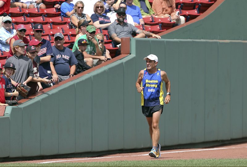 FILE - In this Aug. 23, 2018 file photo, Dave McGillivray, race director of the Boston Marathon, runs past fans inside Fenway Park, as he commemorates the last leg of his 80-day run in 1978 to benefit the Jimmy Fund, before a baseball game in Boston. A few months later, McGillivray underwent triple bypass surgery after suffering chest discomfort and difficulty breathing while running. He is cautioning people thinking of running a marathon to talk with their doctors before hitting the road, especially if they have coronary artery disease or a family history of it. (AP Photo/Elise Amendola, File)
