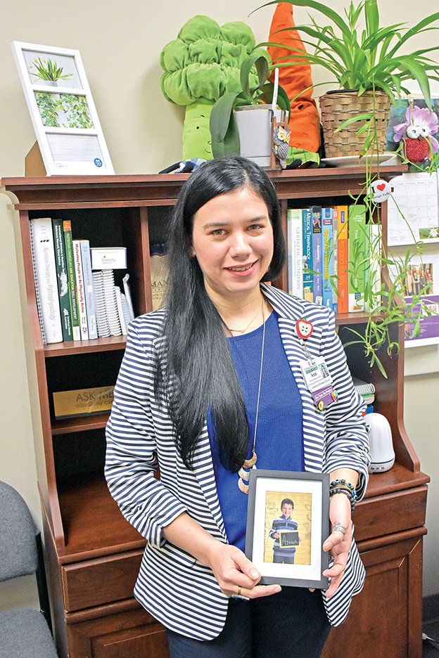 Anni Fuenmayor holds a photograph of her son, Agustin, 9, who was diagnosed with high-functioning autism when he was 4. A wellness/diabetes educator at Conway Regional Medical Center, she wants people to be aware that every child with the disorder is unique. She purchased pins in the shape of a puzzle piece, the symbol of autism, for her co-workers.