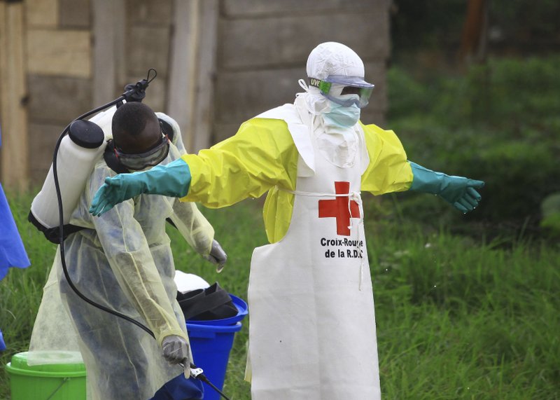 FILE - In this Sunday, Sept 9, 2018 file photo, a health worker sprays disinfectant on his colleague after working at an Ebola treatment center in Beni, eastern Congo. (AP Photo/Al-hadji Kudra Maliro, File)