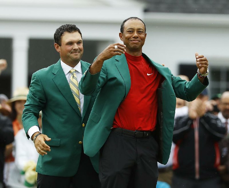 Defending champion Patrick Reed helps Woods put on the green jacket.