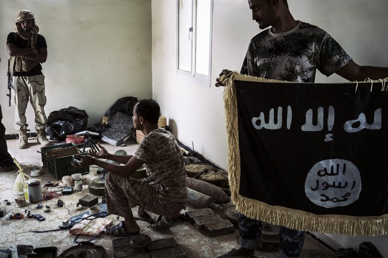 A bomb-disposal specialist who is affiliated with the Shabwani elite forces, an armed group aligned with a coalition led by Saudi Arabia and the UAE, kneels in a seized depot that contains explosive devices made by al-Qaida militants. Another soldier holds an ISIS flag. MUST CREDIT: Photo for The Washington Post by Lorenzo Tugnoli