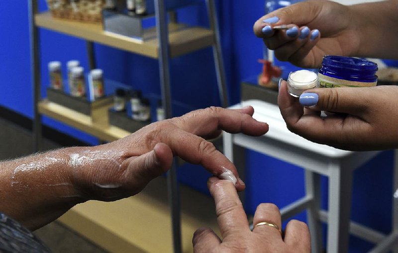 A customer tries a free sample of a cannabidiol (CBD) product labeled as pain cream for her arthritis at Minnesota Hempdropz in Maplewood, Minn. Popularity of CBD products has skyrocketed even though the touted health benefits have drawn skepticism.