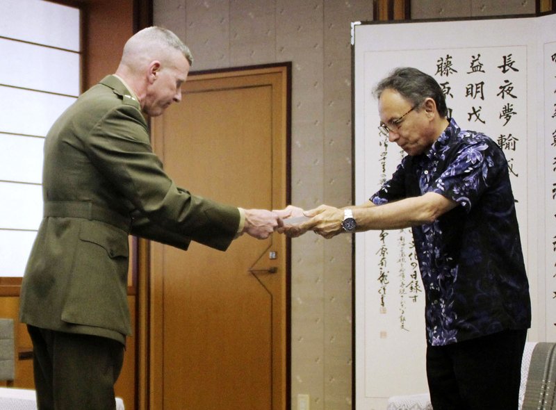Okinawa Gov. Denny Tamaki, right, hands out a letter of protest to Lt. Gen. Eric Smith, U.S. Marines commander in Japan, at Okinawa Prefectural Government Office in Naha, Okinawa, Japan, Monday, April 15, 2019. The commander is asking service people on the southwestern region of Okinawa to keep a low profile to show respect after a sailor allegedly stabbed a Japanese woman and then killed himself. (Kyodo News via AP)