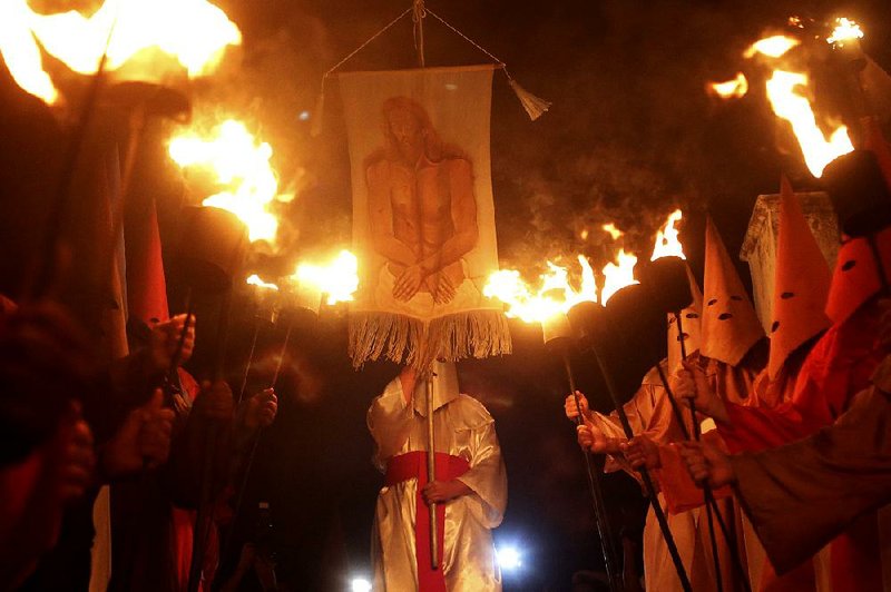 A hooded penitent holds an image of an arrested Jesus Christ during the Procession of Torches, a Holy Week procession Thursday in Goias, Brazil. The procession is a re-enactment of Christ’s arrest by the “farricocos,” men who dress in colored robes with cone-shaped hats, representing the Praetorian guard. 