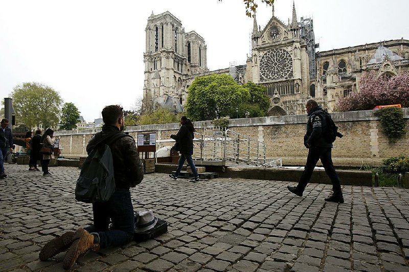 A man kneels as people came to watch and photograph the Notre Dame cathedral after the fire in Paris on Tuesday . Experts are assessing the blackened shell of Paris’ iconic Notre Dame cathedral to establish next steps to save what remains after a devastating fire destroyed much of the almost 900-year-old build- ing. With the fire that broke out Monday evening and quickly consumed the cathedral now under control, attention is turning to ensuring the structural integrity of the remaining building. 