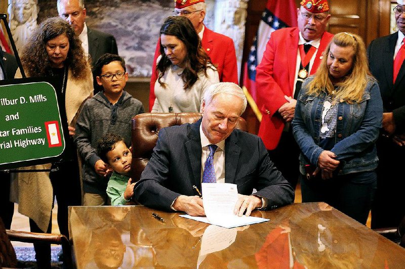 Gov. Asa Hutchinson, surrounded by family members of service- men who died in war zones, signs a bill designating Interstate 630 in Little Rock as a Gold Star Families Highway. 