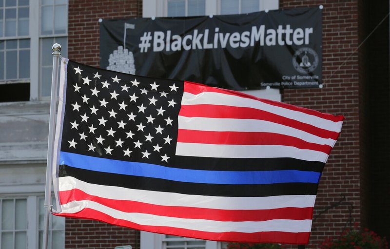 In this July 28, 2016, file photo, a flag with a blue and black stripes in support of law enforcement officers, flies at a protest by police and their supporters outside Somerville City Hall in Somerville, Mass. An Oregon county has agreed to pay $100,000 to a black employee who sued after a co-worker pinned up a "Blue Lives Matter" flag. The Oregonian/OregonLive reports Saturday, April 20, 2019, that Karimah Guion-Pledgure alleged in her January lawsuit that the flag demeans the "Black Live Matter" movement. (AP Photo/Charles Krupa, File)