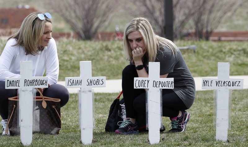 Cassandra Sandusky, right, a graduate of Columbine High School, pauses on Saturday, April 20, 2019, with her friend, Jennifer Dunmore, at a row of crosses bearing the names of the victims of the attack at the school in Littleton, Colo., 20 years ago before a program for the victims. (AP Photo/David Zalubowski)