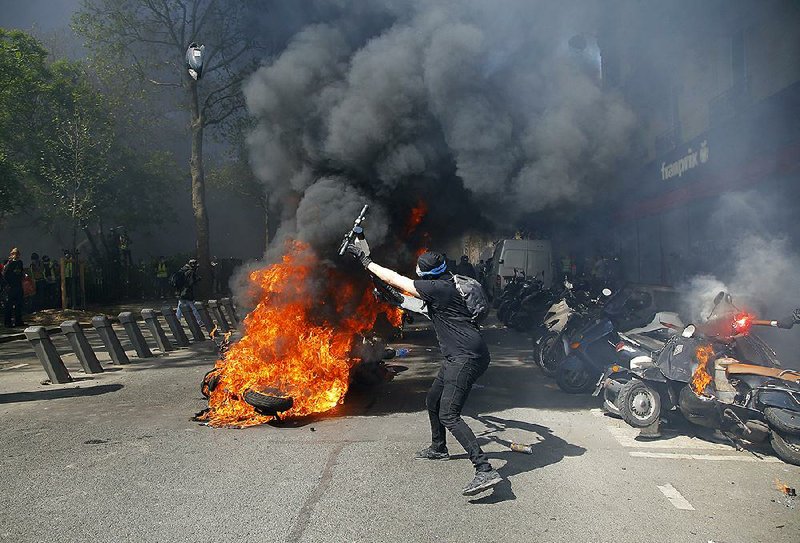 A protester throws a scooter onto a pile of burning motorbikes during Saturday’s demonstration in Paris. 