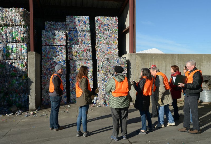 File Photo/NWA Democrat-Gazette/ANDY SHUPE Justin Taylor (from left) and Taylor Gladwin, environmental educators with the Boston Mountain Solid Waste District, speak Dec. 11 with residents beside giant bales of aluminum cans while touring the city of Fayetteville's solid waste and recycling transfer station. New recycling and trash rates in the city begin Monday.