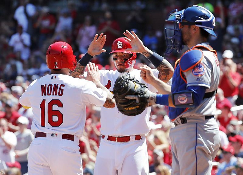 Kolten Wong (left) and teammate Yadier Molina of the St. Louis Cardinals celebrate after scoring past New York Mets catcher Travis d’Arnaud during the second inning Sunday in St. Louis. The Cardinals won 6-4.