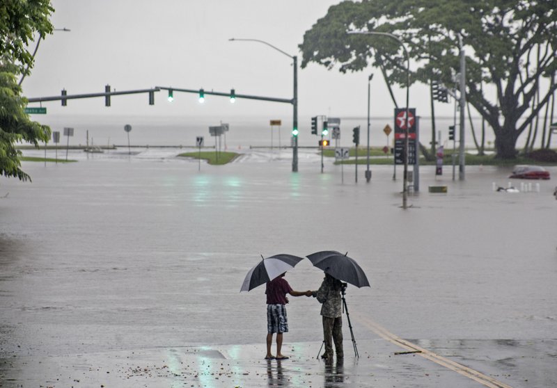 In this Aug. 23, 2018 file photo, people stand near flood waters from Hurricane Lane in Hilo, Hawaii. Some of Hawaii's most iconic beaches could soon be underwater as rising sea levels caused by global warming overtake its white sand beaches and bustling city streets. That&#x2019;s alarming for a state where beach tourism is the primary economic driver.  (Hollyn Johnson/Hawaii Tribune-Herald via AP, File)