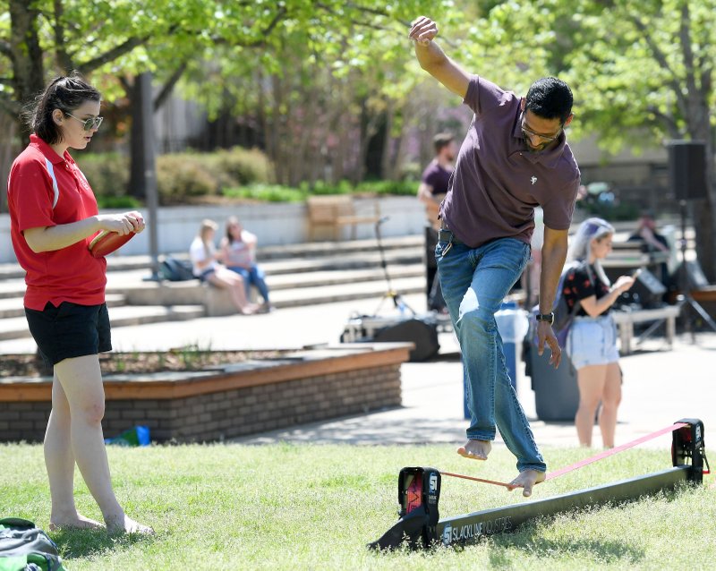 NWA Democrat-Gazette/J.T. WAMPLER Aravind Galla (right) tries a slackline Monday while Hayley Felkins gives pointers during an Earth Day Block Party at the University of Arkansas in Fayetteville. Activities included sand art, information booths presenting facts about sustainability and free succulents to take home. The event was presented by the UA Office of Sustainability. Felkins was supervising the slackline for Urec Outdoors.