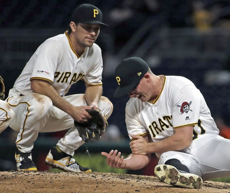 Pittsburgh Pirates relief pitcher Nick Burdi, right, holds his arm after delivering a pitch during the eighth inning of a baseball game against the Arizona Diamondbacks in Pittsburgh, Monday, April 22, 2019. Burdi left the game with a team trainer, and the Diamondbacks won 12-4. (AP Photo/Gene J. Puskar)