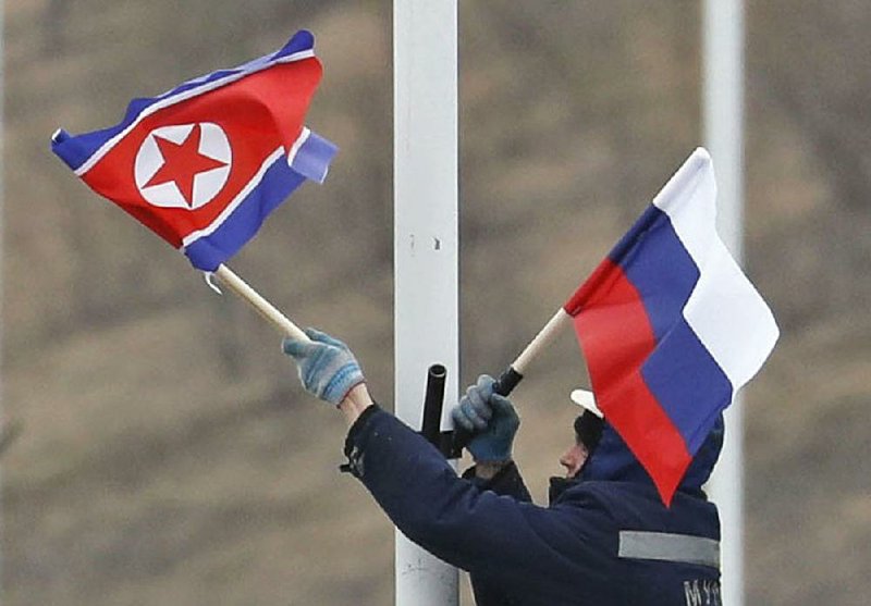 A worker adjusts North Korean (left) and Russian flags Tuesday along a road on Russky Island, off south Vladivostok, a Pacific port city in Russia, where preparations are underway for a summit between the two nations’ leaders. 