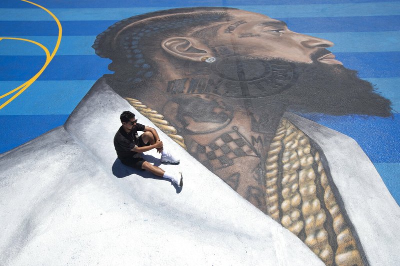 In this April 17, 2019 photo, mural artist Gustavo Zermeno Jr. poses for photos on a basketball court mural he dedicated to slain rapper Nipsey Hussle in Los Angeles. More than 50 colorful murals of Hussle have popped up in Los Angeles since the beloved rapper and community activist was gunned down outside his clothing store. (AP Photo/Jae C. Hong)