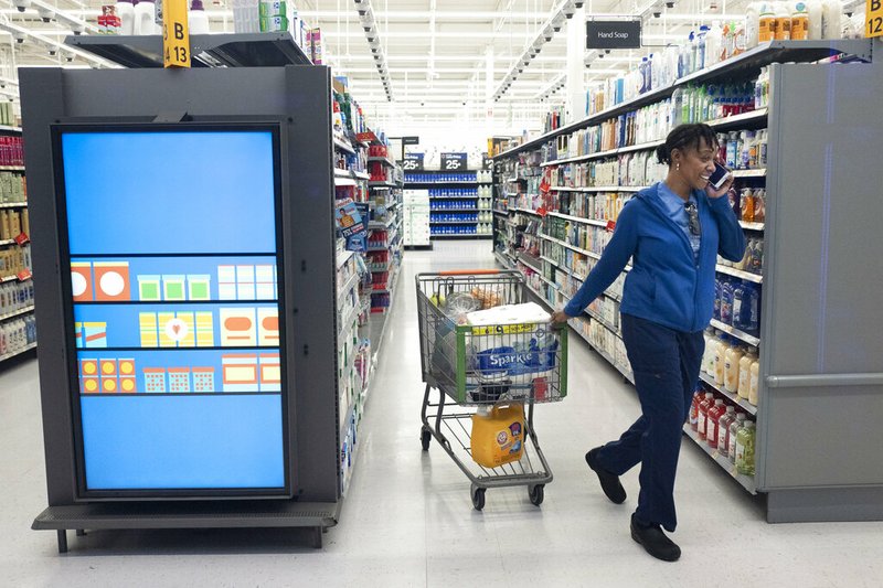 A customer pulls her shopping cart past an information kiosk at a Walmart Neighborhood Market, Wednesday, April 24, 2019, in Levittown, N.Y. Kiosks and signs throughout the store keep customers informed that they are shopping in an artificial intelligence factory. (AP Photo/Mark Lennihan)