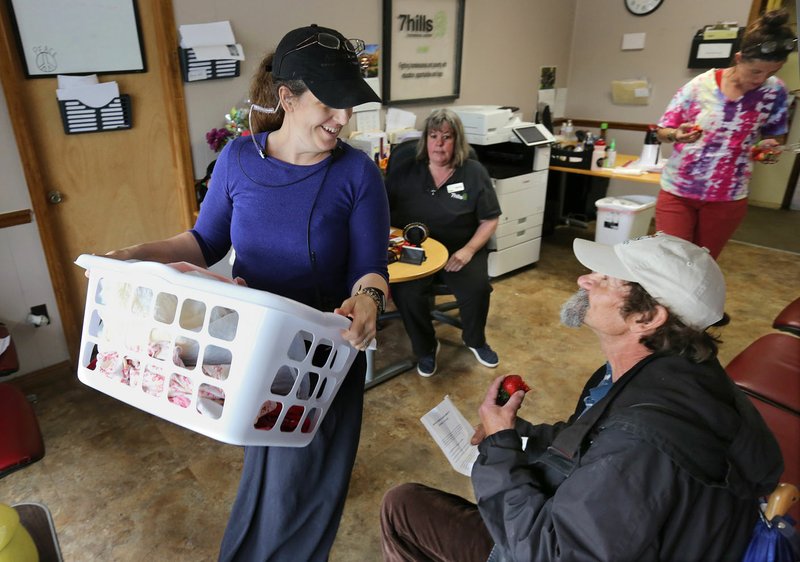 NWA Democrat-Gazette/DAVID GOTTSCHALK Kim Roberson (left), client service specialist at 7 Hills Homeless Center, visits Thursday with Kenneth Lanier as she passes through with folded laundry at the center in Fayetteville. Angel investors in February paid off the remaining debt on the day center's mortgage, allowing 7 Hills to dedicate more money to programming.