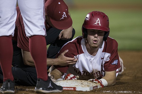 Arkansas designated hitter Matt Goodheart is examined by trainer Corey Wood during the Razorbacks' game against Tennessee on Friday, April 26, in Fayetteville.
