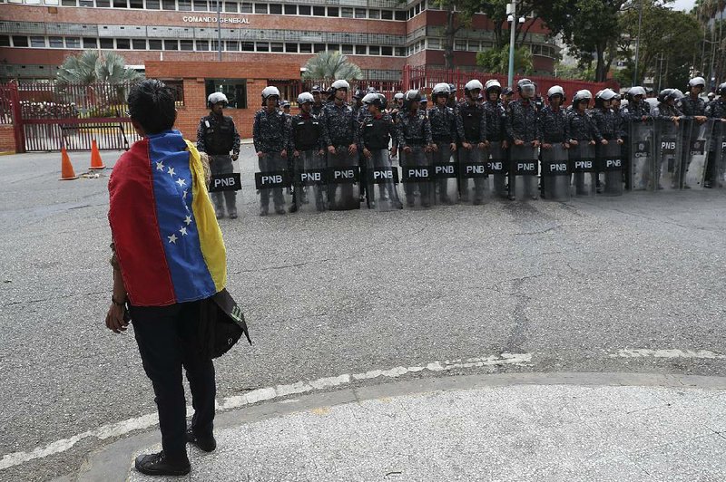 An opponent of Venezuelan President Nicolas Maduro protests Saturday outside the navy’s command headquarters in Caracas as  police officers form a protective line. Opposition leader Juan Guaido had urged Venezuelans to go to military garrisons and other  official buildings to make the case against Maduro. 