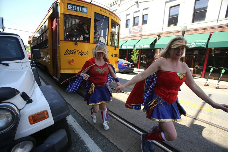 Geneva Lamm (right) and Gina Pharis (left), dressed as Wonder Woman, run away after &quot;stopping&quot; a trolley on President Clinton Avenue on April 10 while promoting May 11th's DC Wonder Woman Run Series. (Arkansas Democrat-Gazette/THOMAS METTHE)