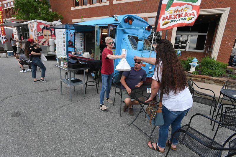 NWA Democrat-Gazette/J.T. WAMPLER Trenton Cargill (LEFT) of Springdale hands an order to Stephany Bley and her husband Chris Bley of West Fork Thursday May 2, 2019 during First Thursday on the Fayetteville square. The Fayetteville city council is considering a ban on expanded polystyrene foam packaging in food trucks and concessionaires on city owned property. 