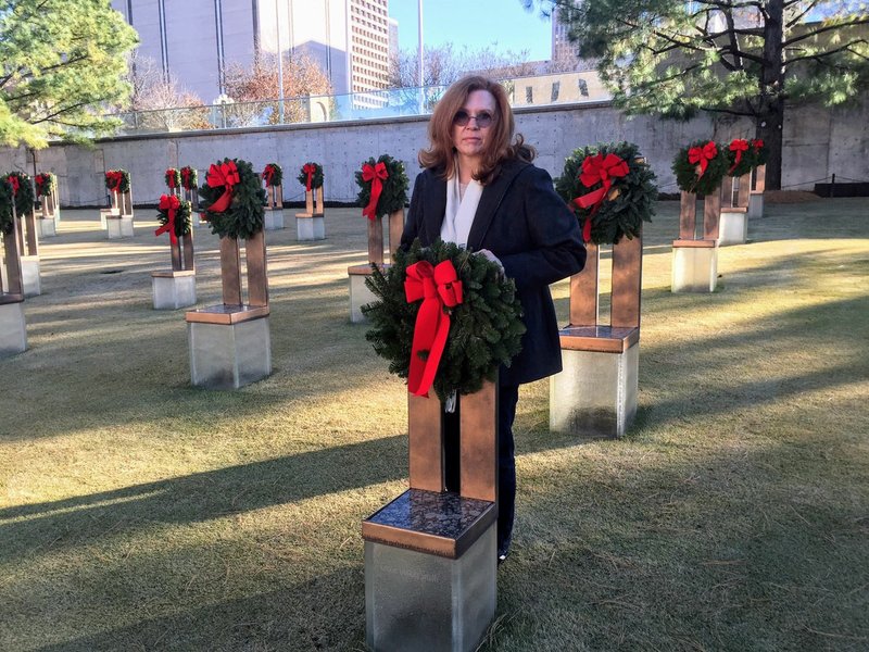 Special to Arkansas Democrat-Gazette Kathy Sanders stands behind the chair placed in memory of her grandson, Chase Smith, who, with his brother, Colton, were among the 168 people killed in the Oklahoma City bombing on April 19, 1995. Sanders said she and her husband Tom usually spend Christmas in Oklahoma with family and visit her grandsons' chairs at that time. "I feel like the boys are very much part of my life now, through her," Tom Sanders said. "I can't imagine anybody doing a better job of using what happened to her to help other people."