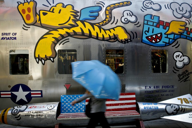 A woman walks by a bench painted with an American flag outside a fashion boutique selling U.S. brand clothing at the capital city's popular shopping mall in Beijing, Monday, May 13, 2019. Companies waited Monday to see how China decides to retaliate for President Donald Trump's latest tariff hike while forecasters warned their escalating fight over technology and trade might disrupt a Chinese economic recovery. (AP Photo/Andy Wong)