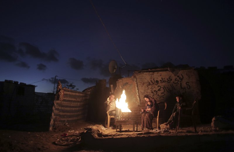 File - In this Jan. 15, 2017 file photo, a Palestinian family warm up outside their makeshift house during a power cut in Khan Younis in the southern Gaza Strip. Qatar's Foreign Ministry said Tuesday, May 7, 2019, that it will send $480 million to Palestinians in the West Bank and the Gaza Strip after a cease-fire deal ended the deadliest fighting between Israel and Palestinian factions since a 2014 war. A statement from Qatar said $300 million would support health and education programs of the Palestinian Authority, while $180 million would go toward &quot;urgent humanitarian relief&quot; in United Nations programs and toward electricity. (AP Photo/ Khalil Hamra, File)