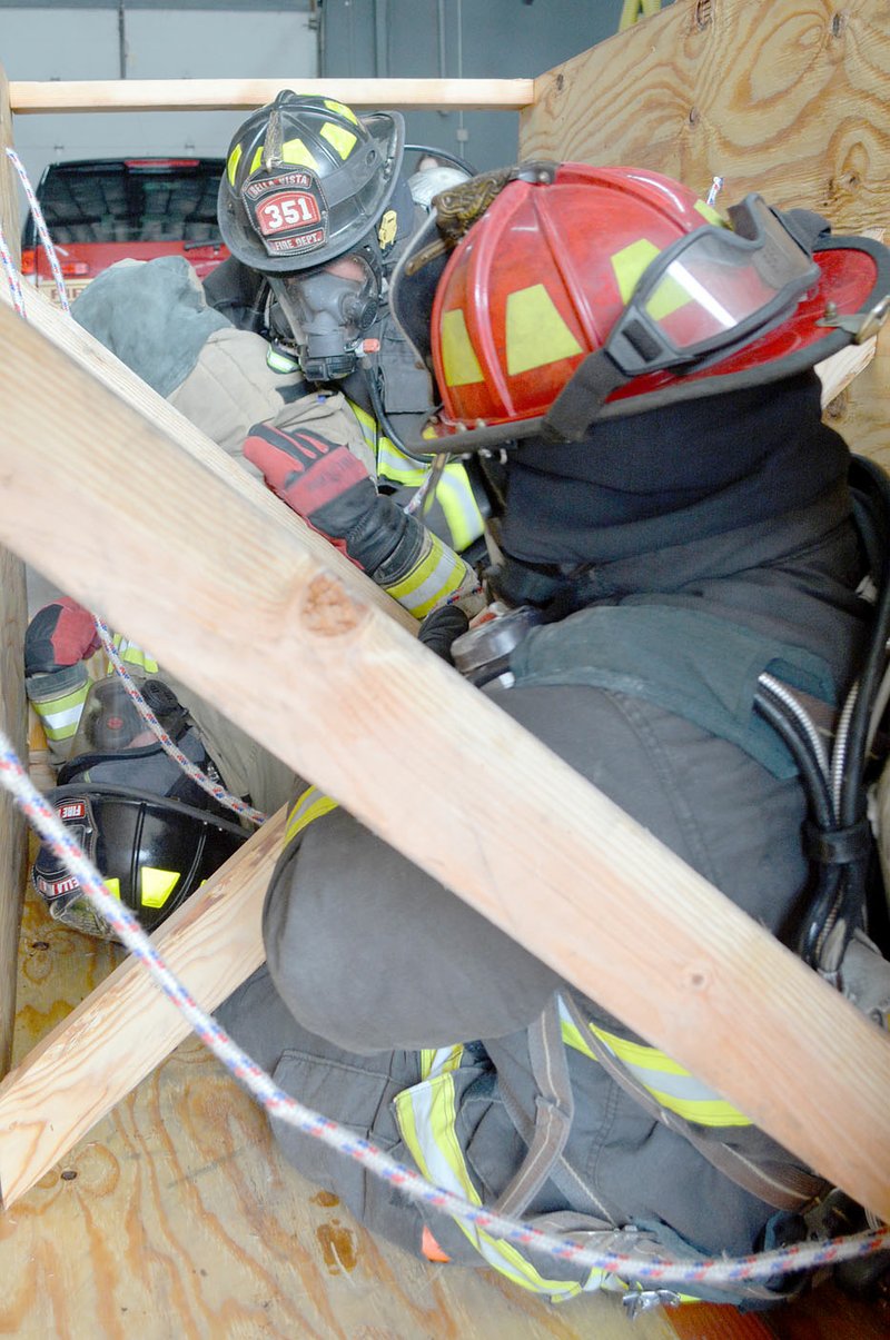 Keith Bryant/The Weekly Vista Capt. Justin Tesreau (foreground) carefully pulls firefighter Tyler Miller, posing as an incapacitated firefighter, through narrow gaps in a wooden training tunnel while firefighter Byron Abernathy lifts him into the tunnel.
