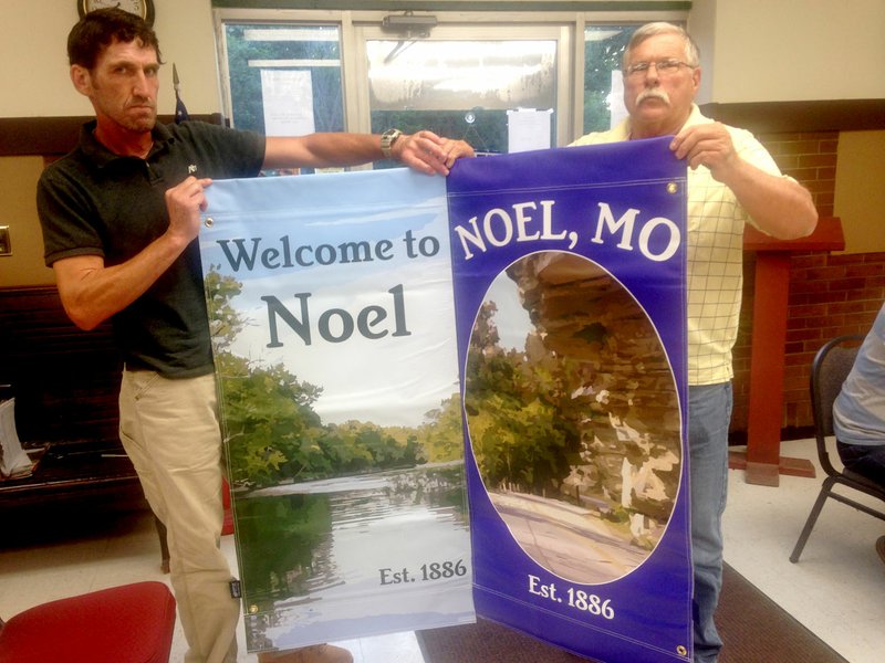 Sally Carroll/McDonald County Press Noel Street Superintendent Chris Craig (left) and Judge Robert Barth show off the two new banner designs that will soon adorn Noel's Main Street. Craig plans to put up about 10 new banners by week's end in an effort to beautify the city and prepare for all the summer visitors.