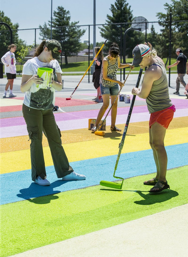 Delia Moyle (left), a junior at Bentonville High School, and Sarah Butcher, a teacher in the Ignite Professional Studies program, help paint a mural Wednesday on the basketball courts at Memorial Park in Bentonville. The mural with a '70s theme was designed by Bentonville High School senior Jonathon Coppick. Digital design and photography students in the School District's Ignite Professional Studies program created designs for each of the four courts representing the 1970s, 1980s, 1990s and 2000s. Students in the program are helping to paint the designs over coming weeks with guidance from Mike Abb with the Runway Group and local muralist Graham Edwards. NWA Democrat-Gazette/BEN GOFF &#8226; @NWABENGOFF